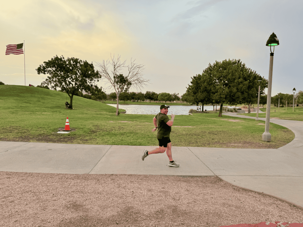 Man jogging in park near lake at sunset.
