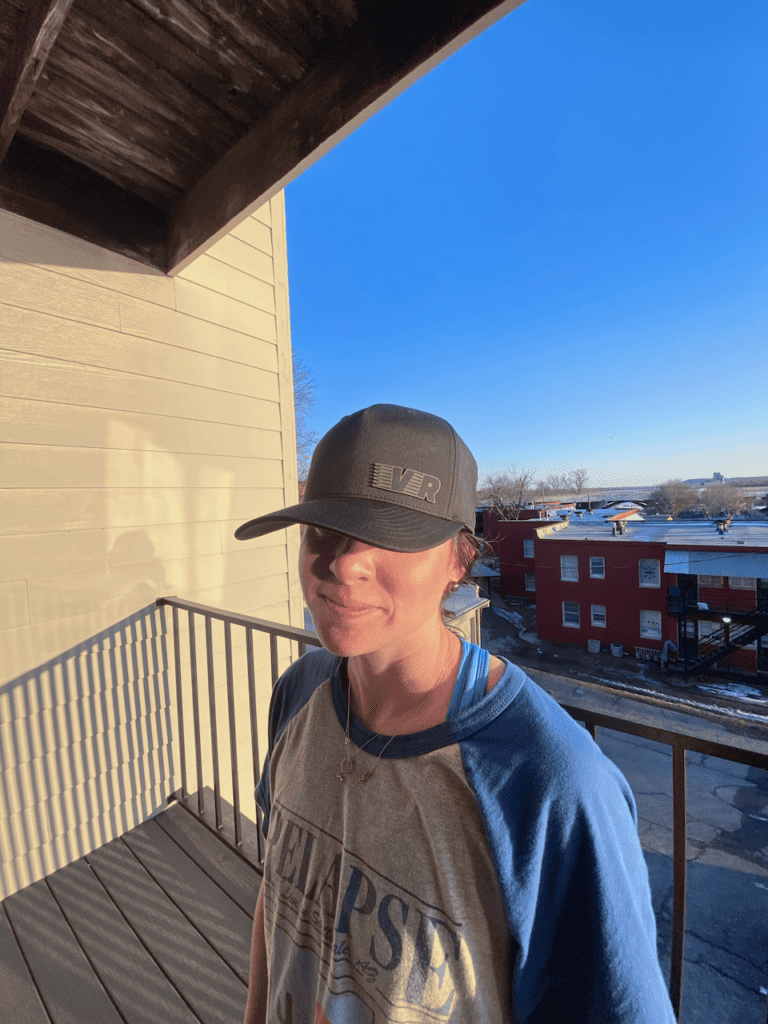 Person smiling on balcony under blue sky.