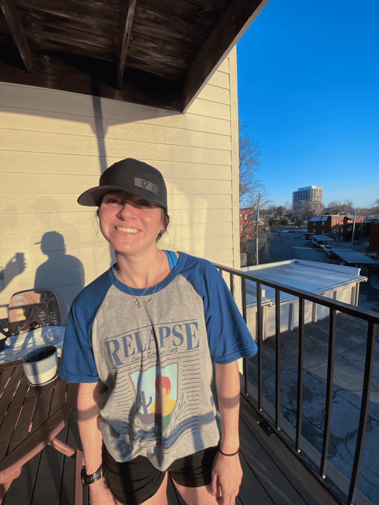 Woman in casual attire smiling on sunny balcony.
